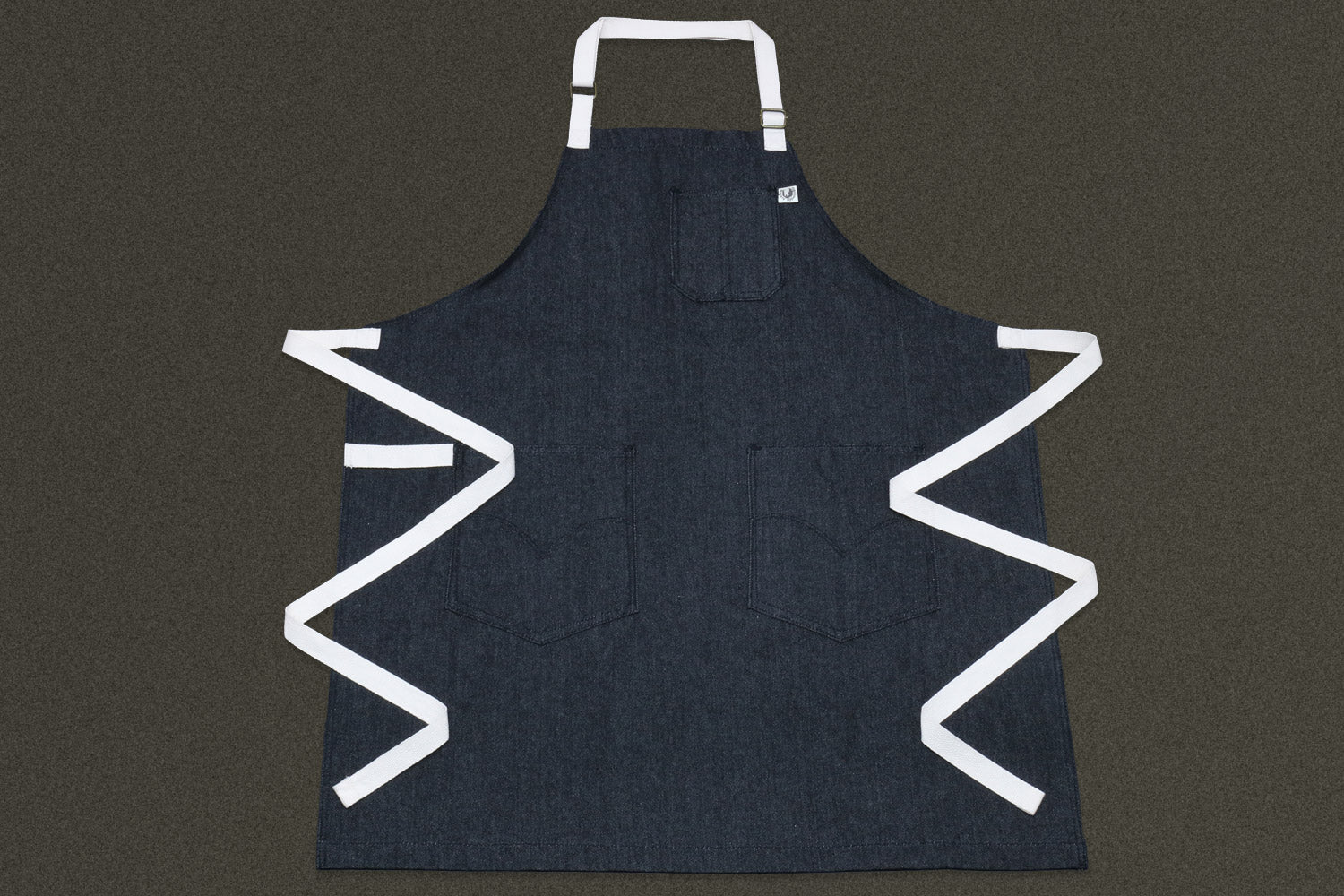 Dark denim kitchen apron with white trim, chest pocket, and deep side pockets