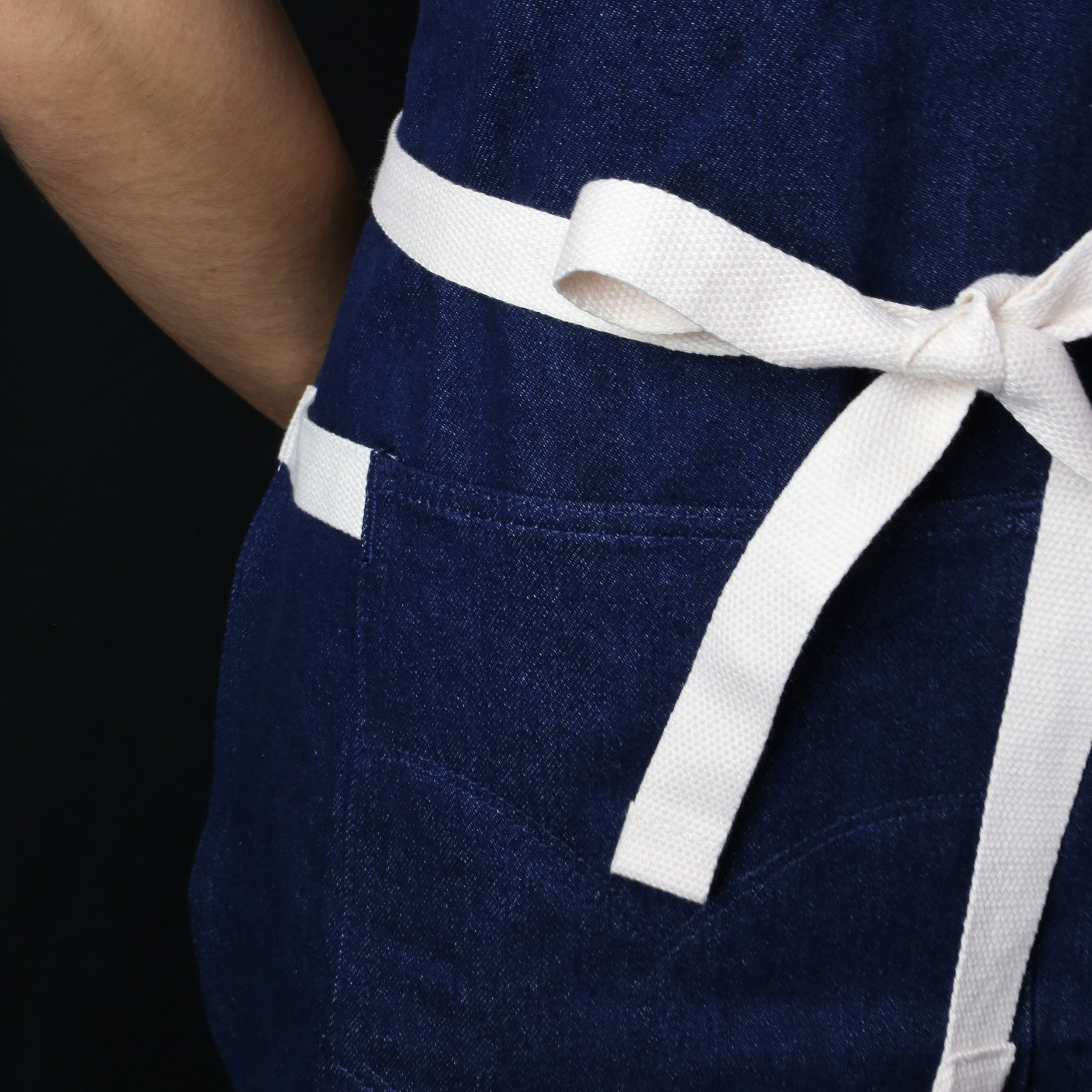 Dark denim apron bib detail with white waist tie and stitched pocket panel