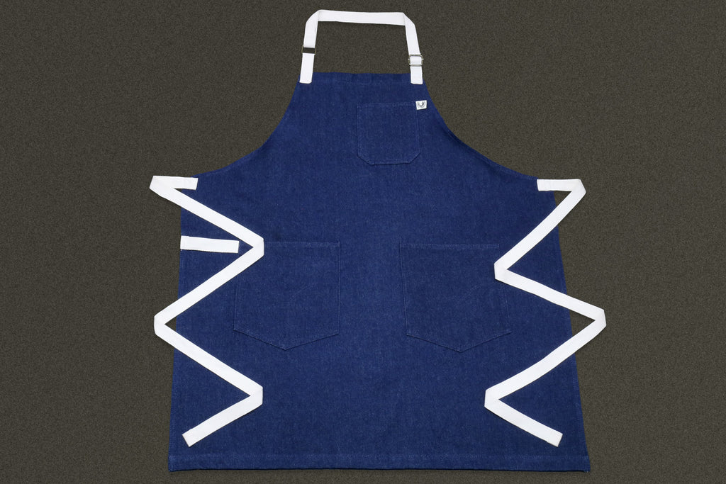 Dark denim kitchen apron front view with white neck strap and waist ties