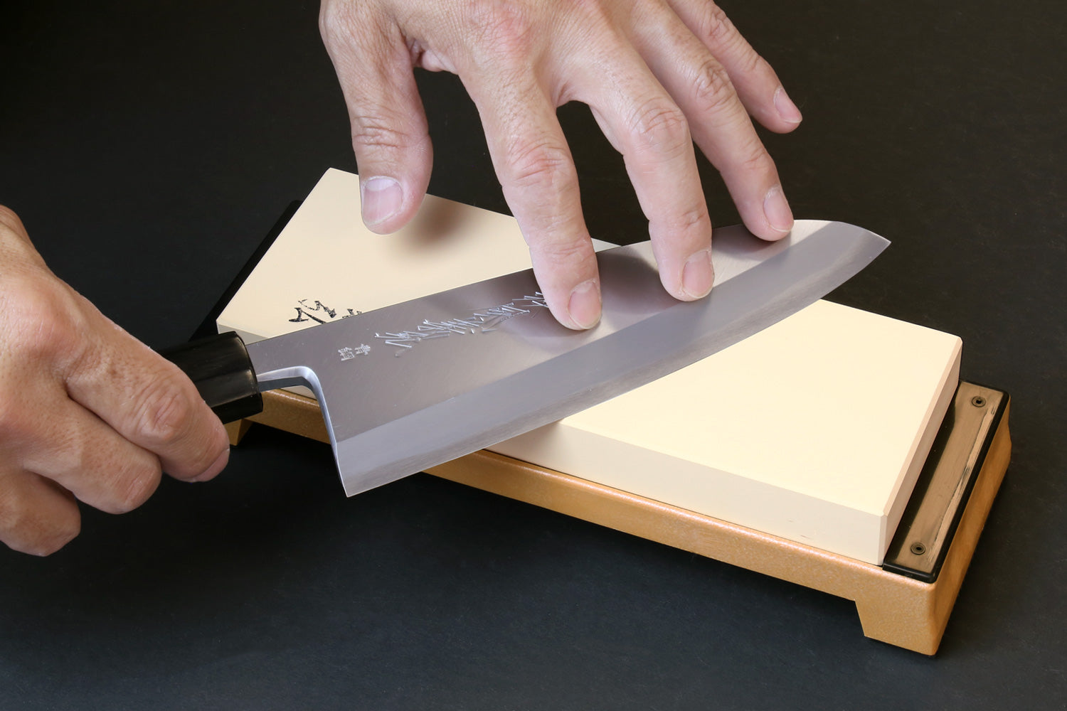 Whetstone 3000 grit on wooden base with hand holding blade over the stone surface
