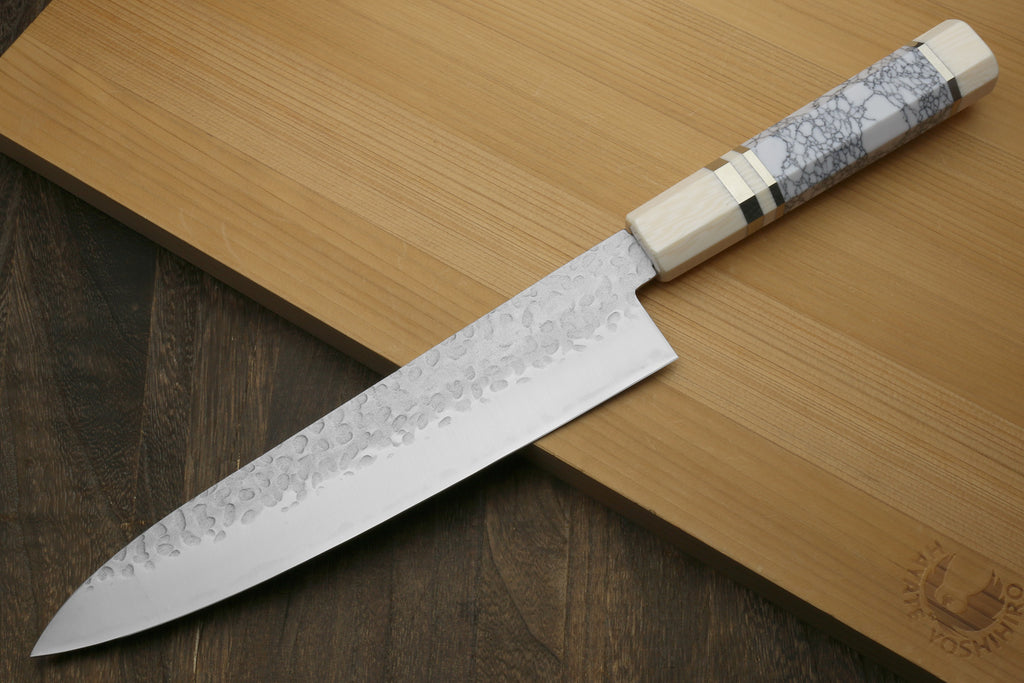 Gyuto chef knife angled on board with hammered stainless blade and white handle