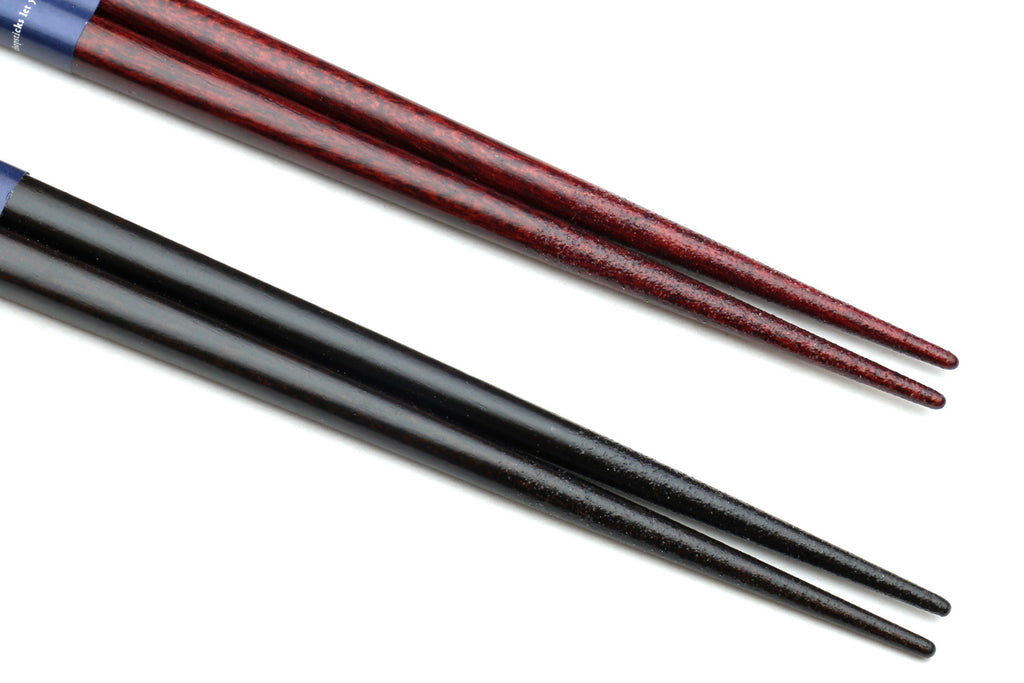 Close-up of lacquered chopsticks, dark finish with red-brown tips.