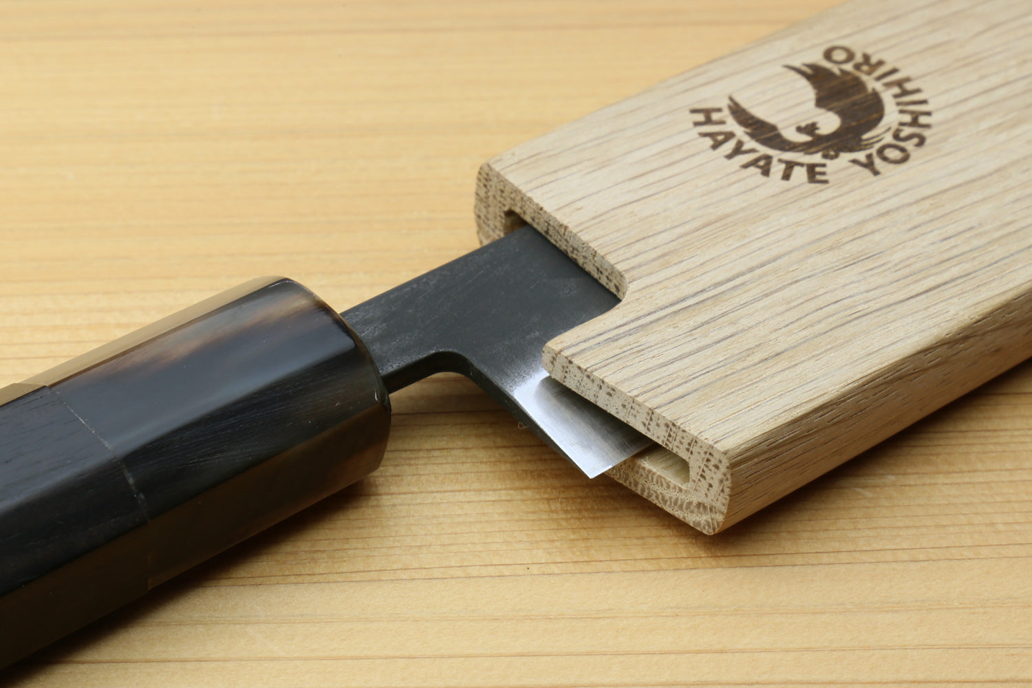 Light oak wooden saya cover with logo, partially fitted over a knife blade