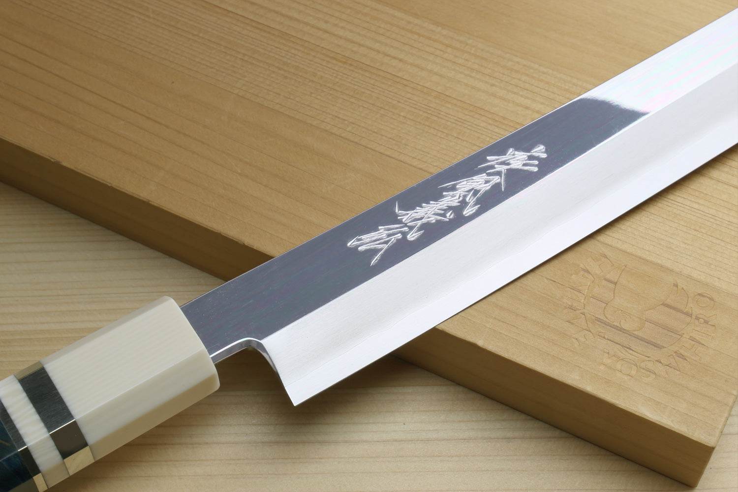 Polished stainless yanagi knife blade showing engraved marks near the bolster