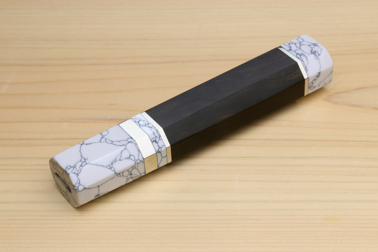 Ebony knife handle with white howlite bolster and gold-tone band, angled view