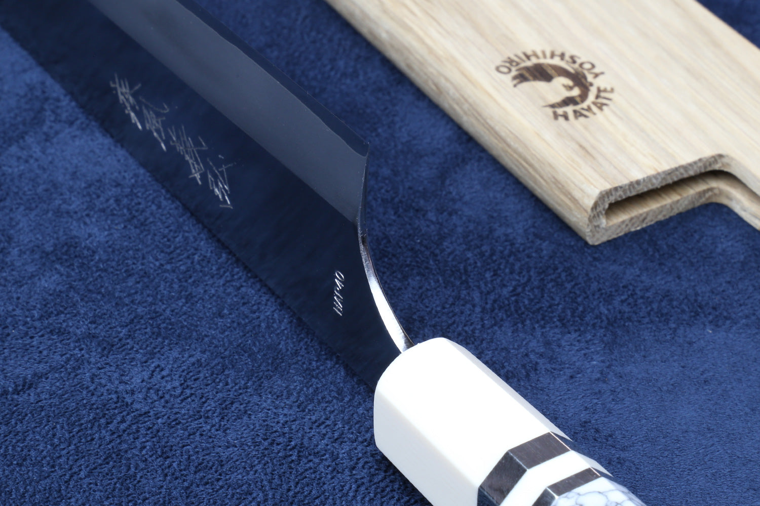 Chef's gyuto knife with dark sheath and ivory-pattern bolster; close-up view.