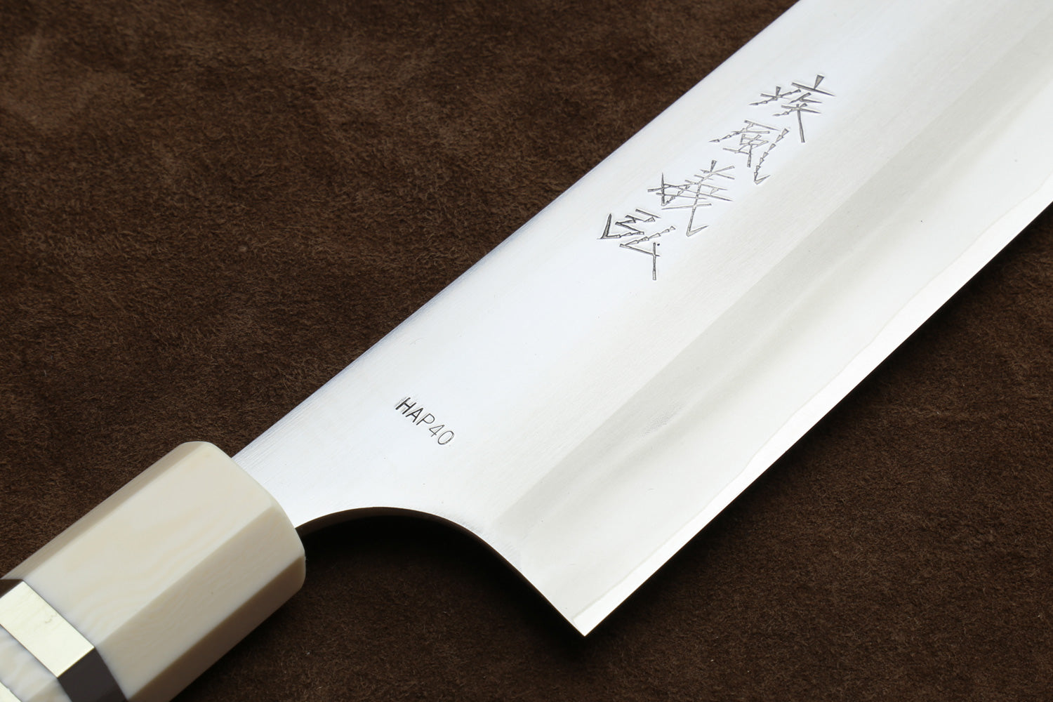 Gyuto chef knife blade close-up with HAP40 marking and octagonal ivory bolster, curved edge