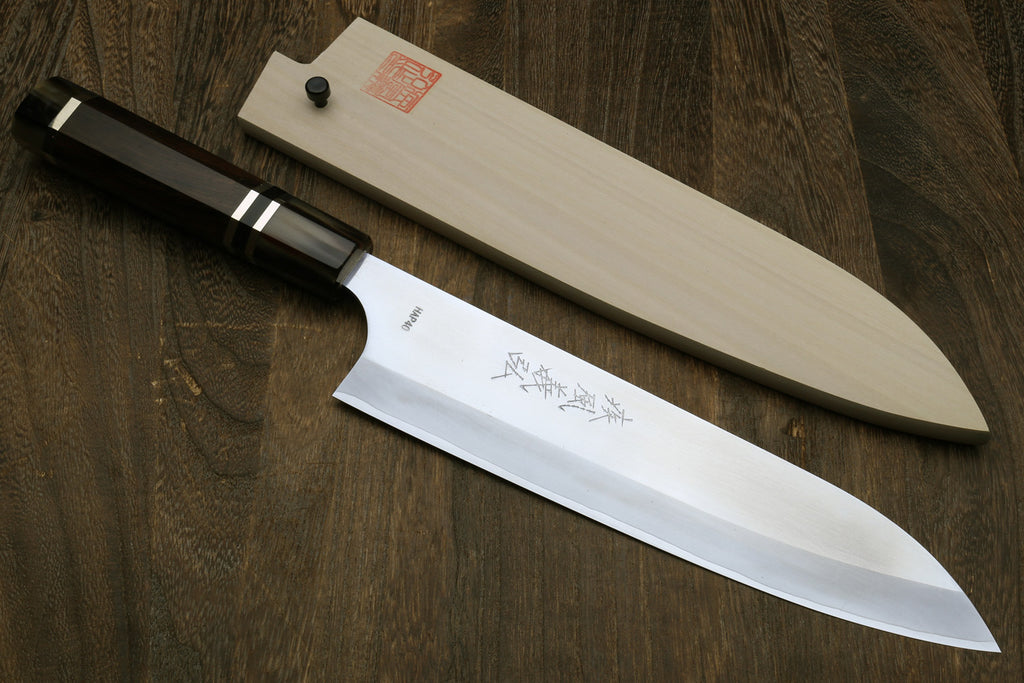 Chef knife laid across a wooden surface with white saya cover
