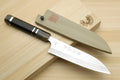 Petty chef knife and whetstone set on wooden board, with dark triple-ring handle