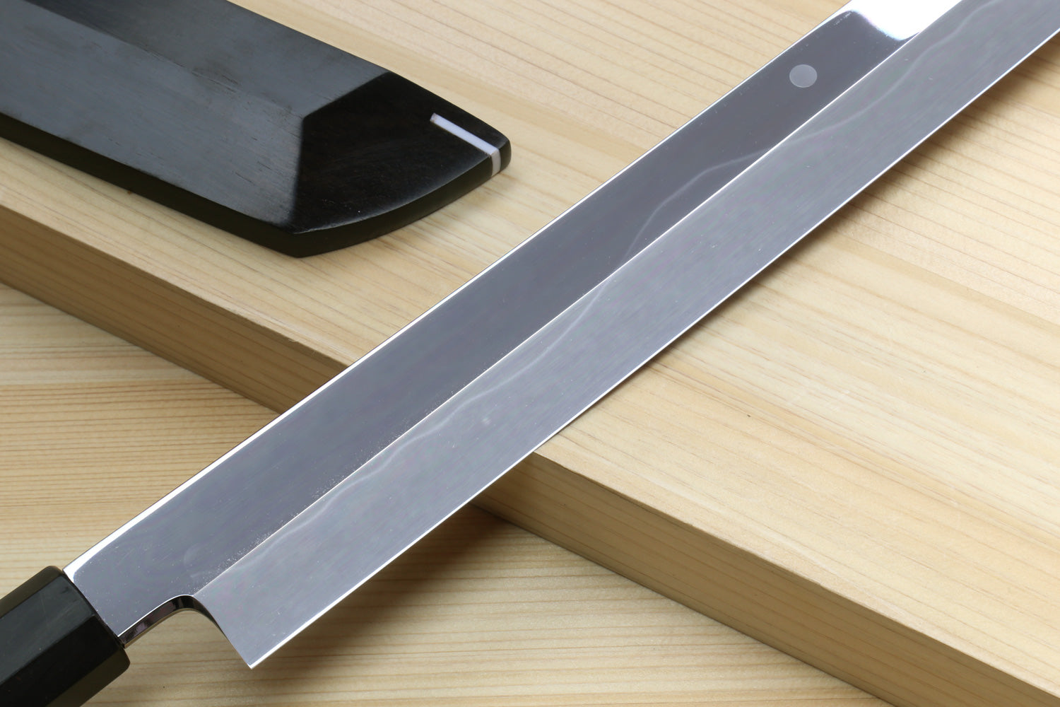 Japanese kitchen knife with silver blade across dark saya on wooden board