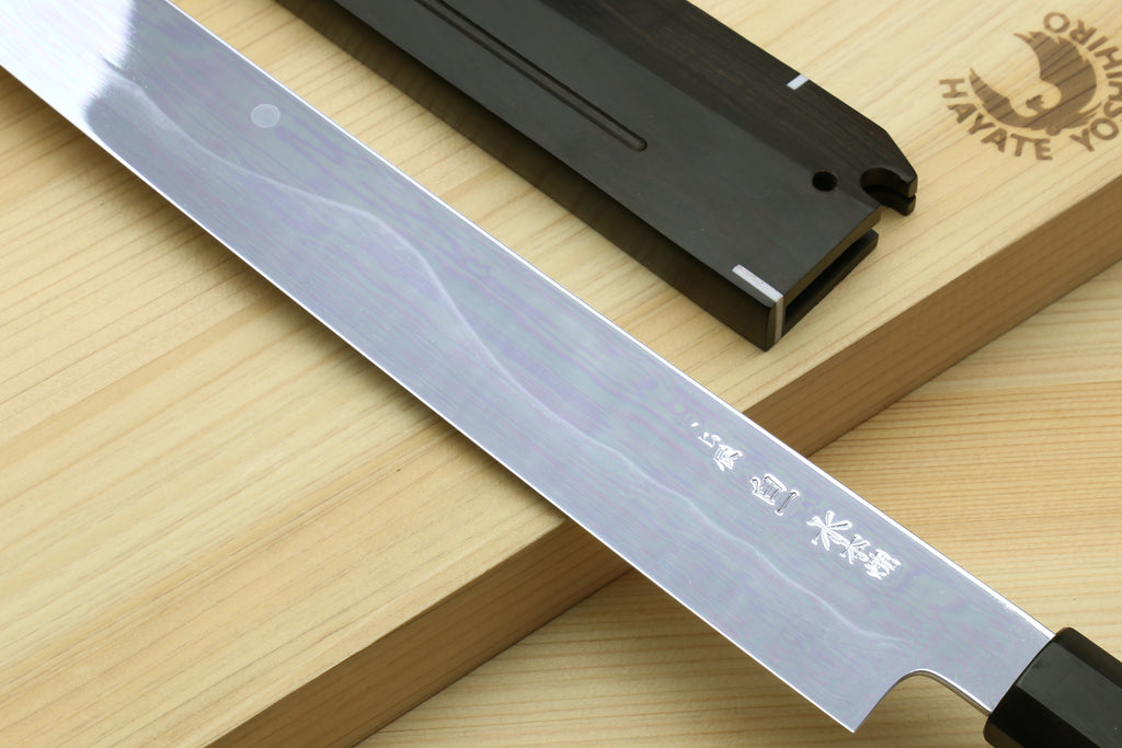 Japanese kitchen knife blade with silver finish and black saya on wooden board