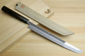 Japanese knife laid beside its saya; mirror-finished blade with dark handle visible.
