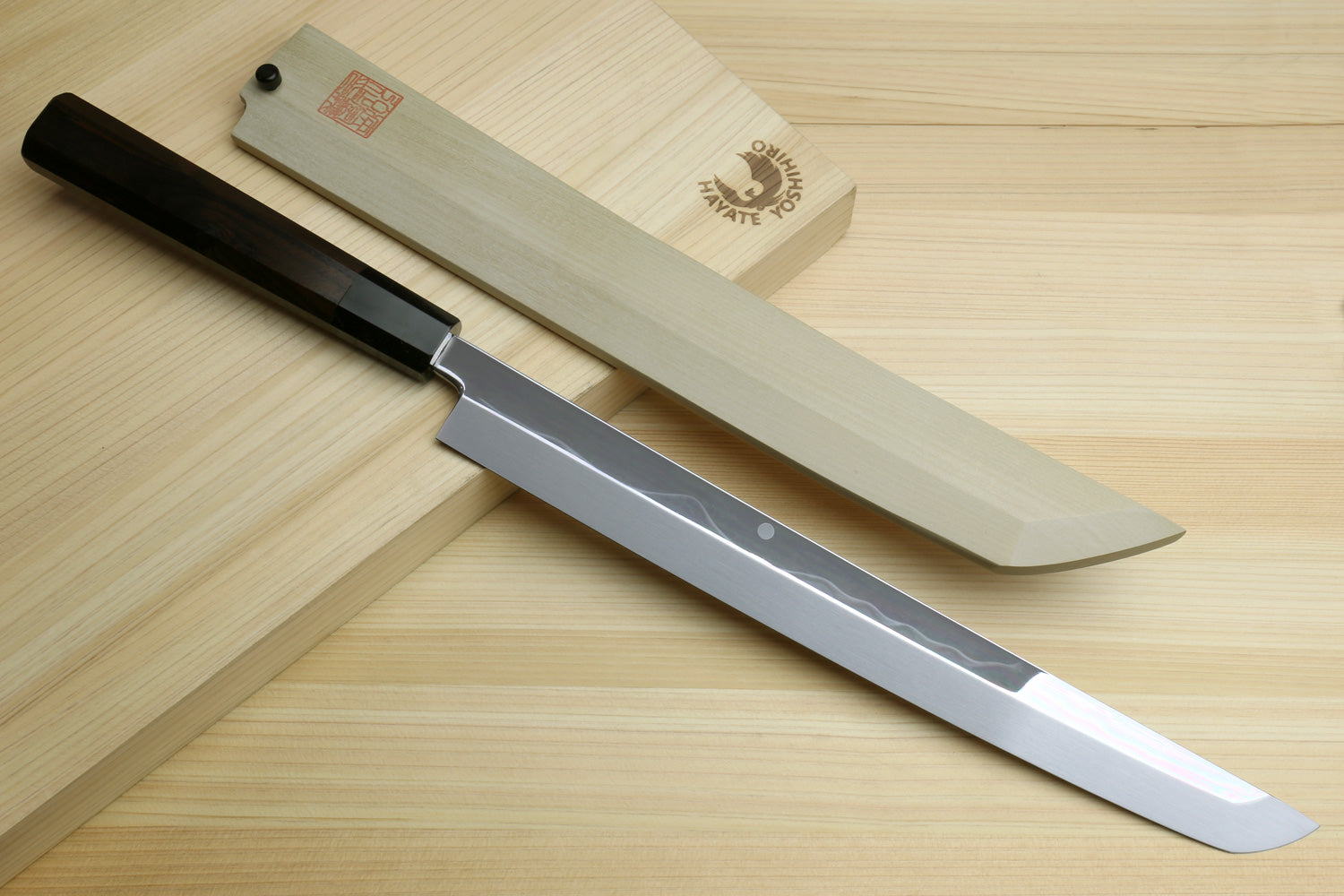 Japanese knife laid beside its saya; mirror-finished blade with dark handle visible.