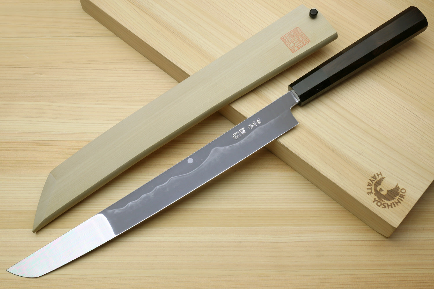 Japanese knife with mirror-finished blade and black handle, with light saya beside it.