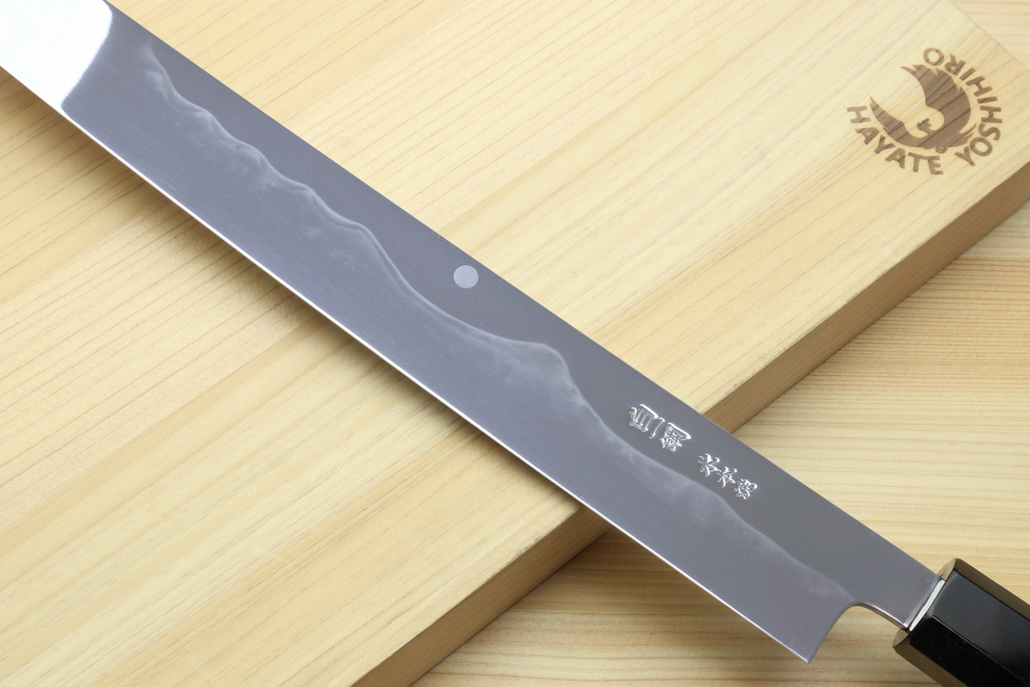 Japanese knife blade close-up with stamped marks and dark handle, saya behind.