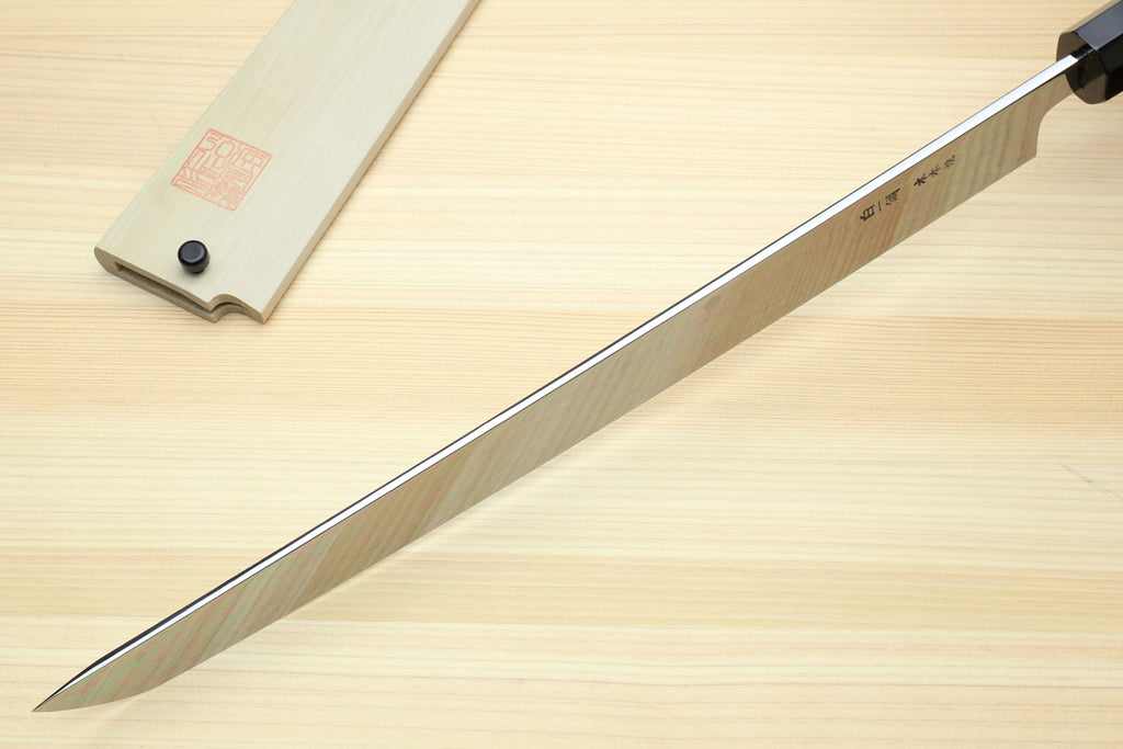 Japanese knife blade in profile with light saya; reflective edge and pointed tip.