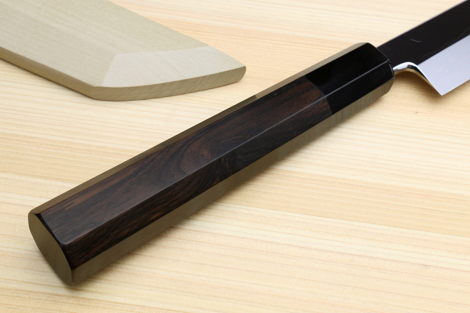 Ebony handle Japanese knife with mirror-finished blade edge visible.
