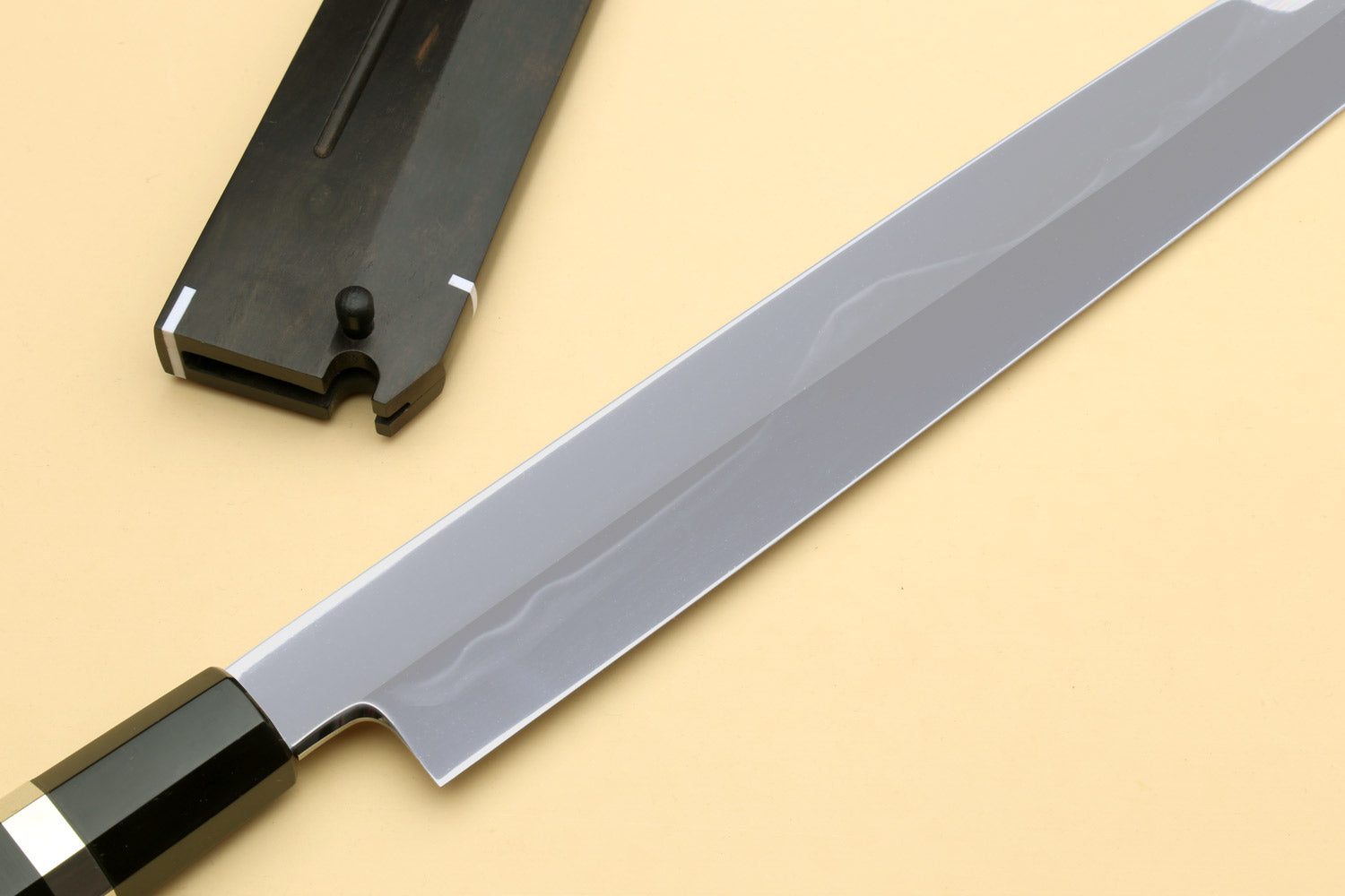 Japanese chef knife with silver blade and black handle, partially in dark sheath