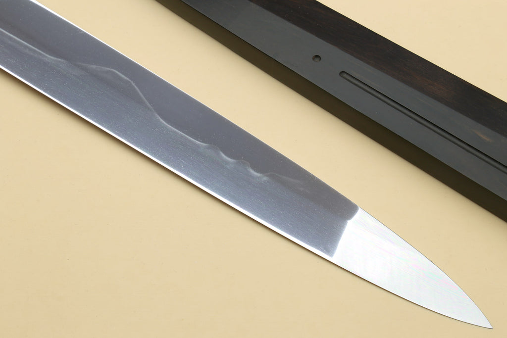 Japanese chef knife blade close-up with wavy hamon pattern and pointed tip