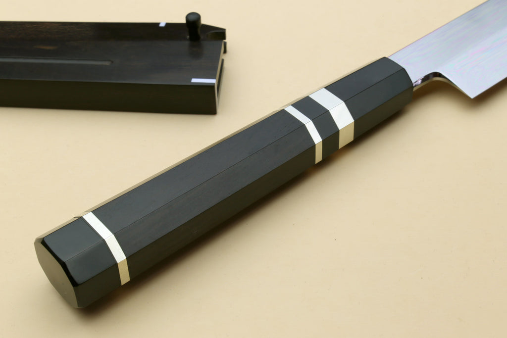 Japanese chef knife with black striped handle and dark sheath behind, angled view