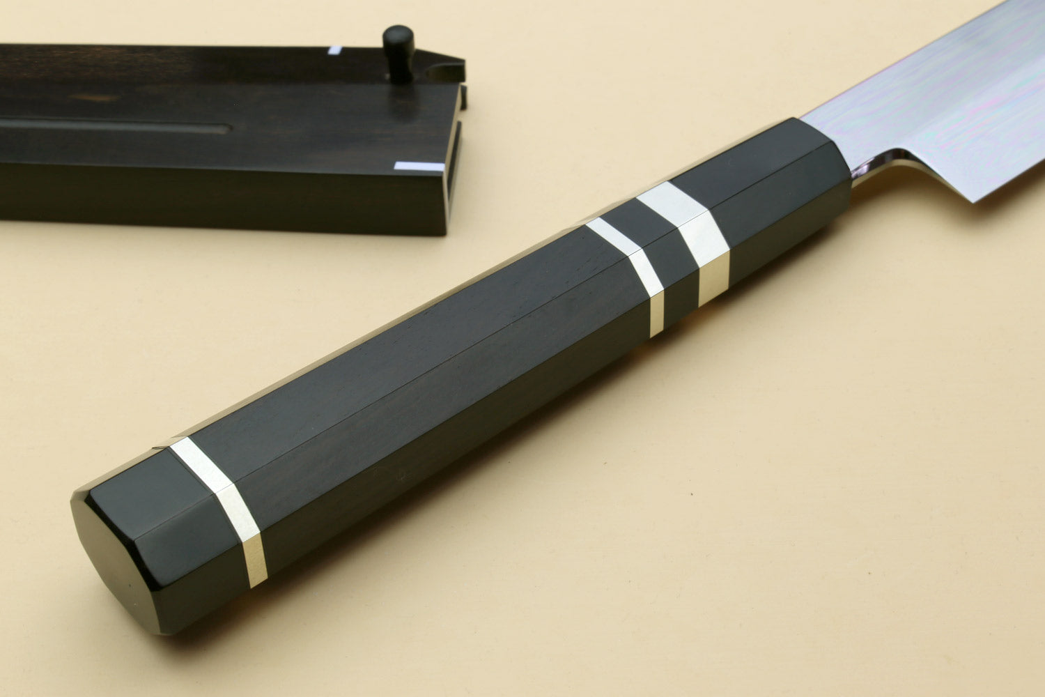 Japanese chef knife with black striped handle and dark sheath behind, angled view