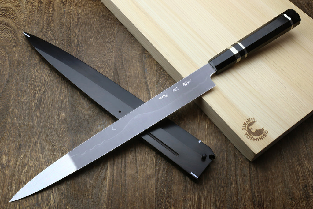 Japanese chef’s knife with mirror-finished steel blade, ebony handle, on wooden board.