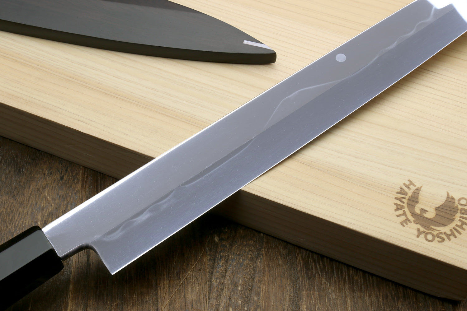 Japanese chef’s knife blade close-up with etched waves and reflective silver finish.