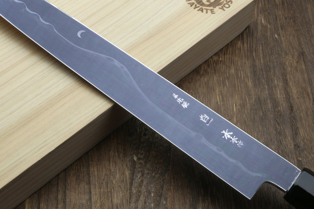 Japanese chef’s knife blade detail with engraved markings and moon-like motif near tip.
