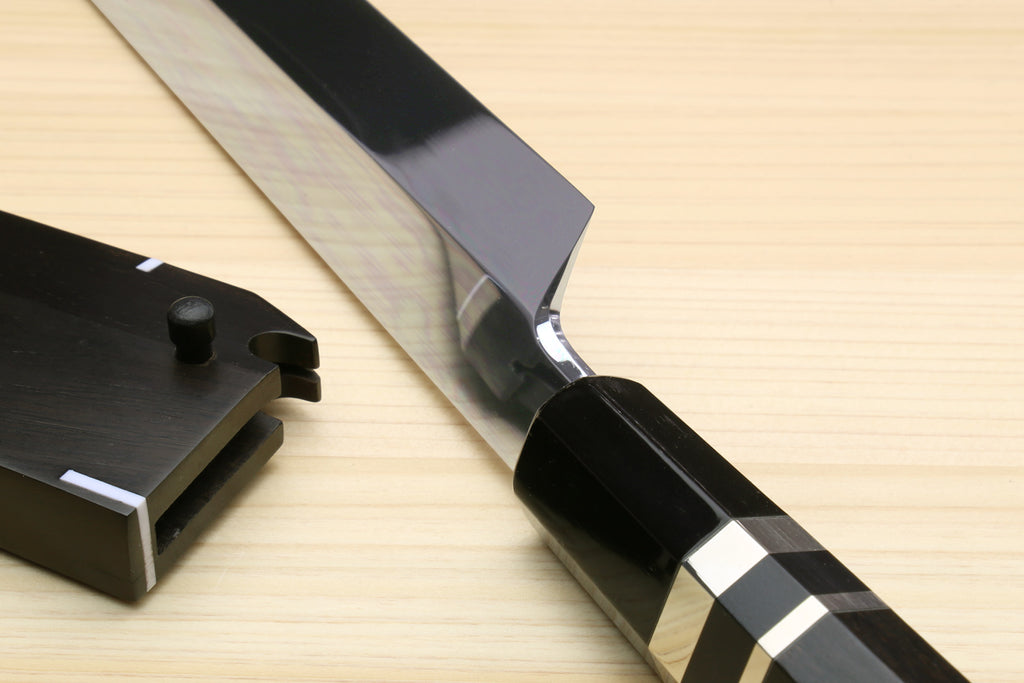 Japanese chef’s knife with ebony handle and silver-striped band, beside black saya case.
