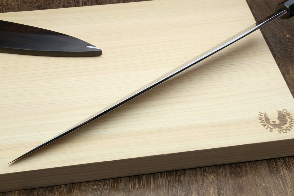 Japanese chef’s knife laid diagonally across wood, mirror blade with dark backing.
