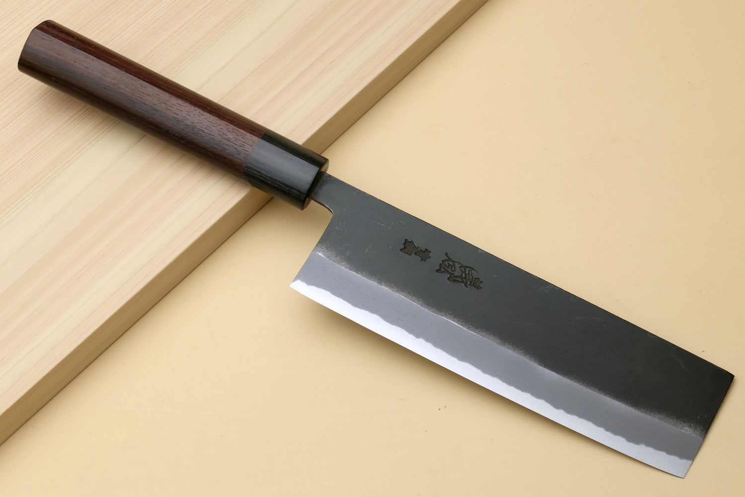 Japanese nakiri vegetable cleaver with dark wood handle and black kurouchi finish blade