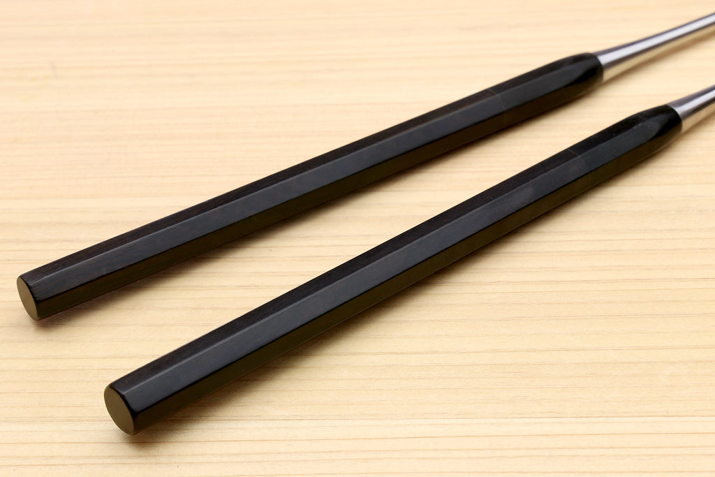 Ebony octagonal handles of plating tweezers with silver metal ends on wood