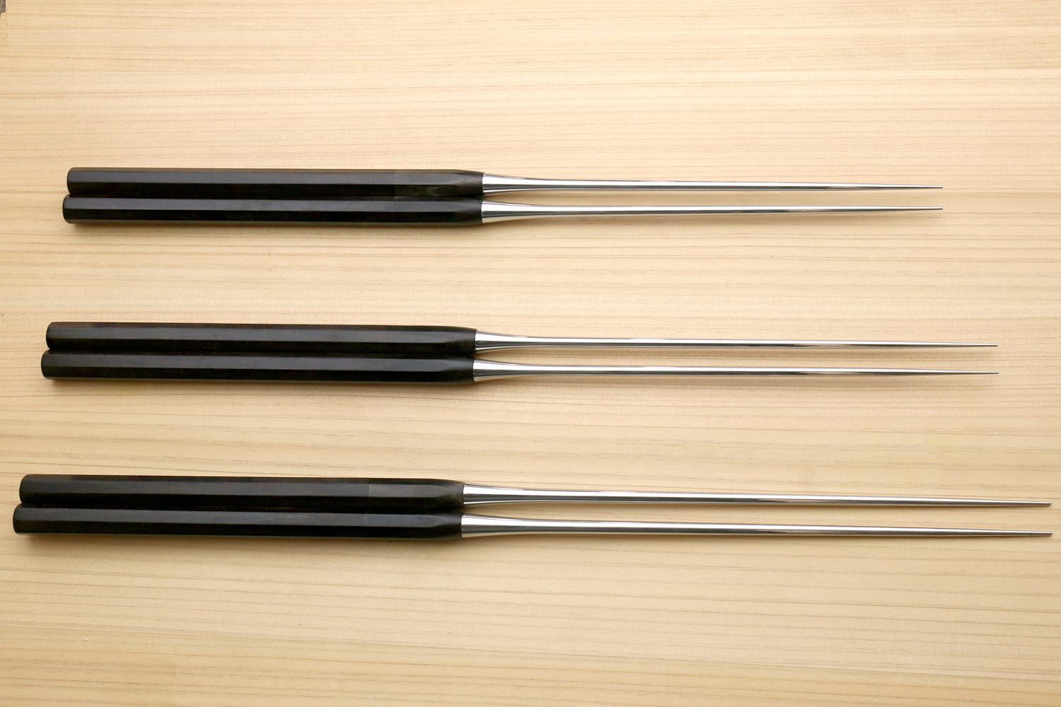 Set of three plating tweezers with ebony handles and stainless metal tips on wood