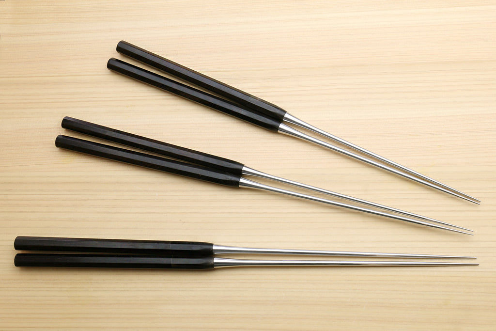 Four plating tweezers with ebony handles and stainless tips arranged on wood