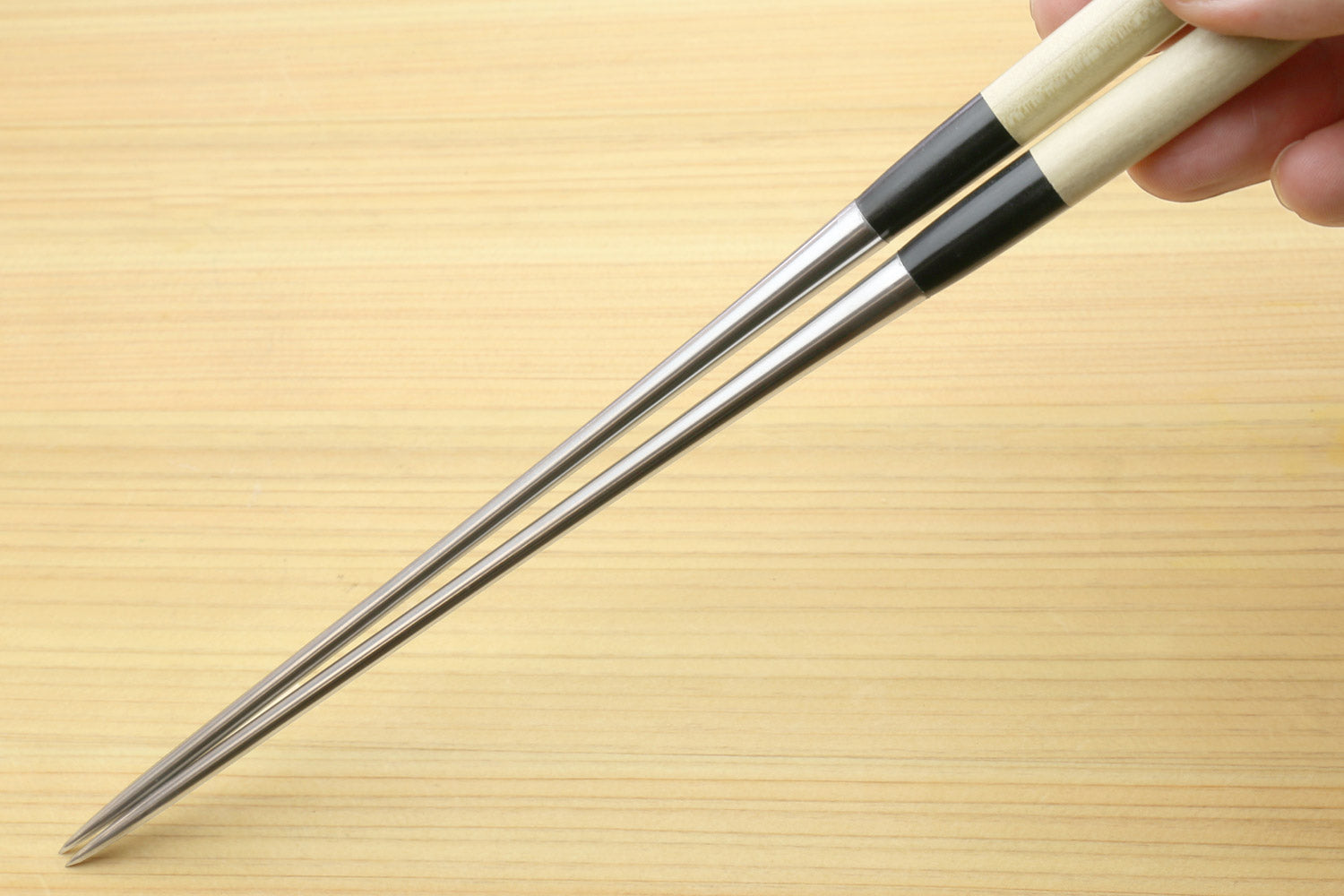 Hand holding sushi plating tweezers with light wood handle and stainless tips