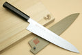 Japanese gyuto chef knife with stainless blade and dark handle on wooden board