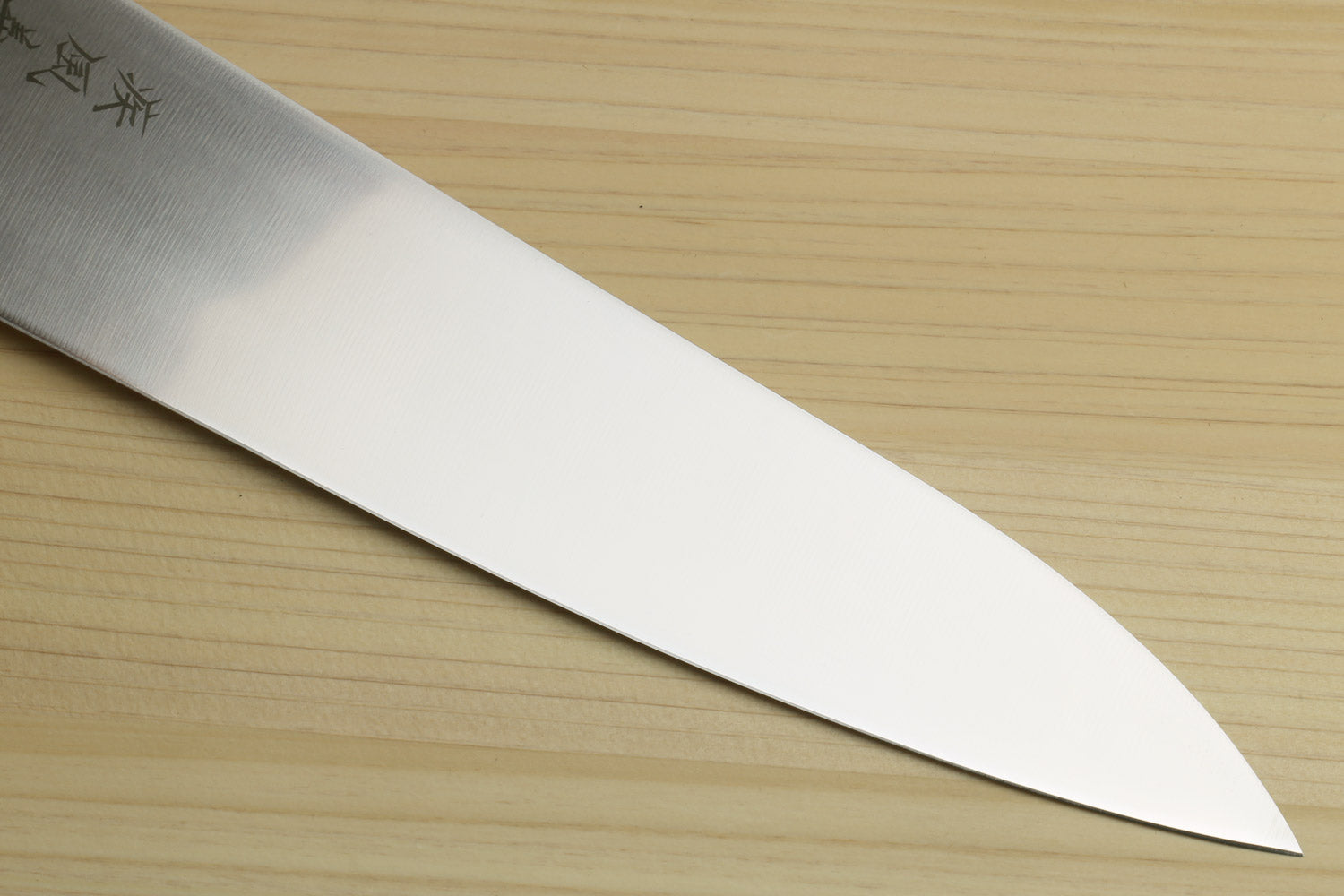 Stainless gyuto chef knife blade close-up with tapered edge and subtle grind lines