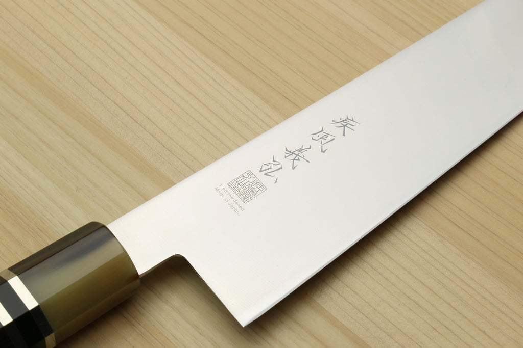Japanese gyuto knife blade close-up with etched markings and dark handle ferrule