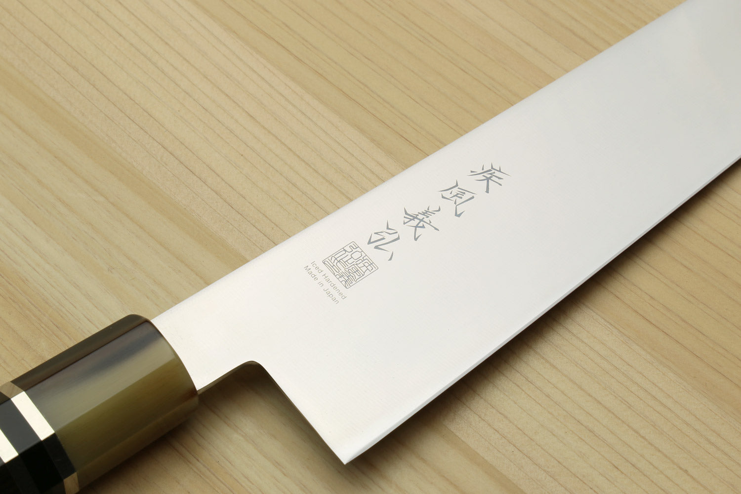 Japanese gyuto knife blade close-up with etched markings and dark handle ferrule