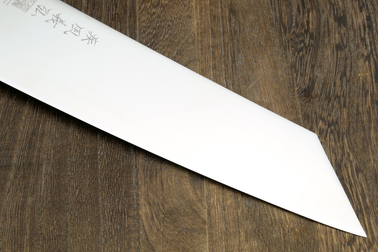 Kiritsuke chef knife blade close-up with etched markings and clean bevel.