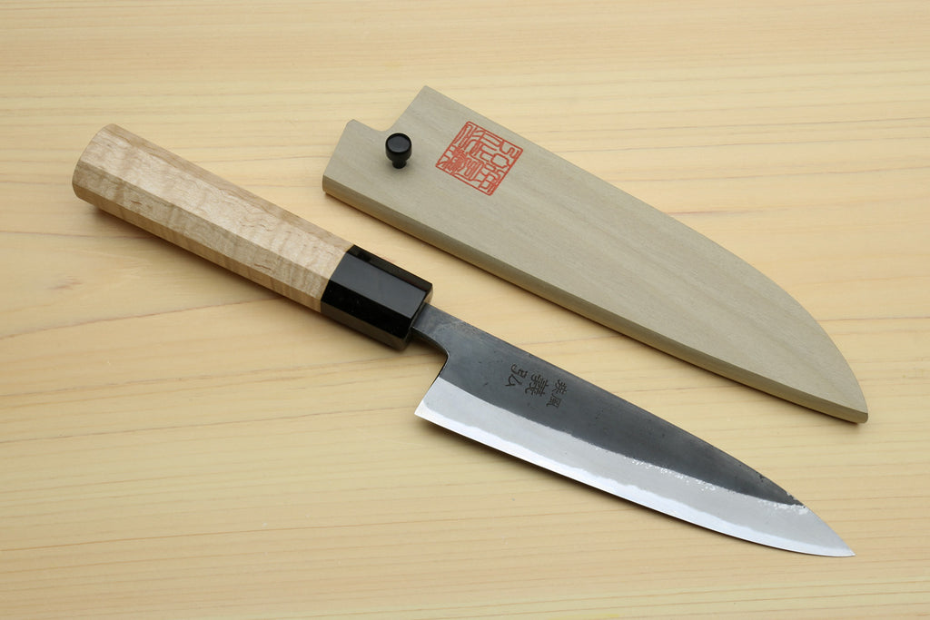 Petty utility knife and saya cover on tabletop, light wood handle with black bolster