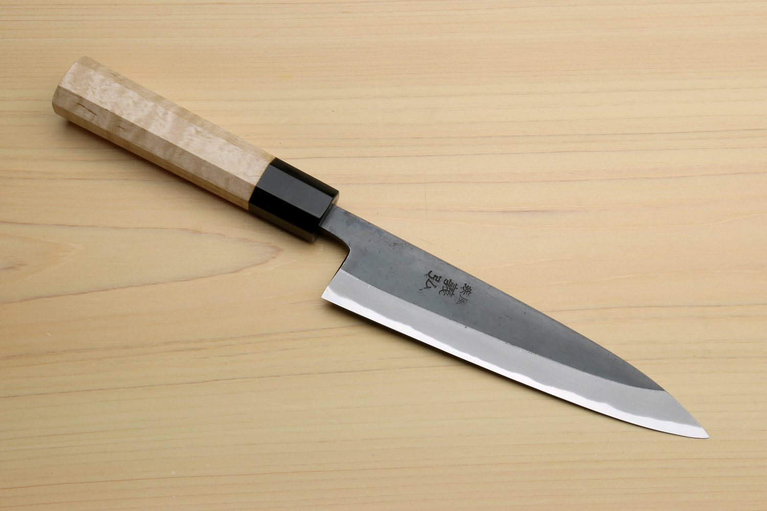 Petty utility knife with dark blade, sharp edge, and light wood handle with black bolster