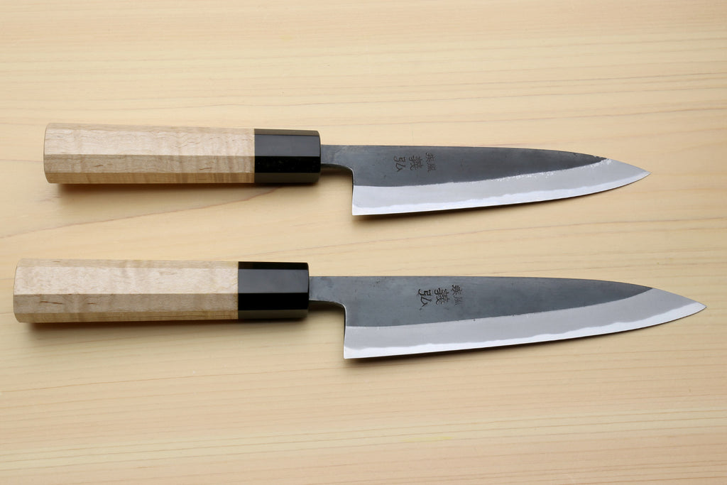 Petty utility knives laid flat, dark blades with light wood handles and black bolster