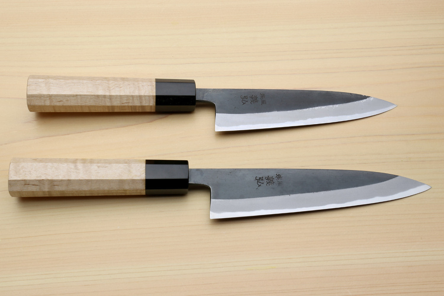 Petty utility knives laid flat, dark blades with light wood handles and black bolster