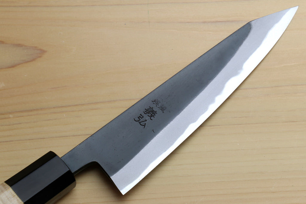 Kurouchi-finished blue steel knife blade with visible engraved mark and light edge.