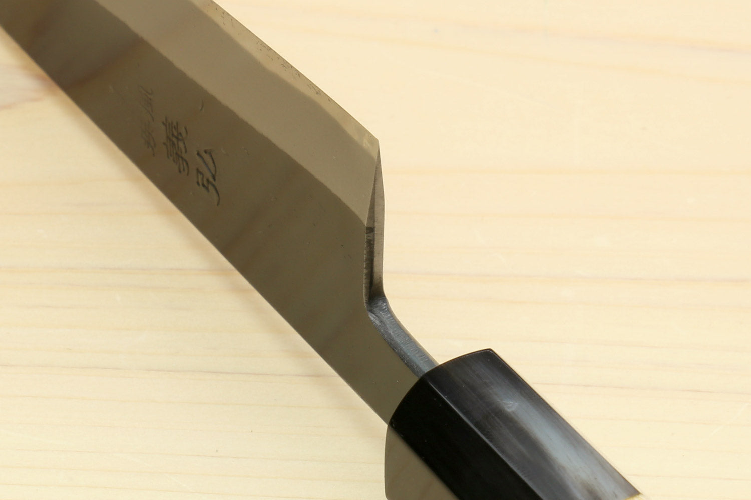 Kurouchi-finished blue steel knife tip and side profile with dark handle bolster.