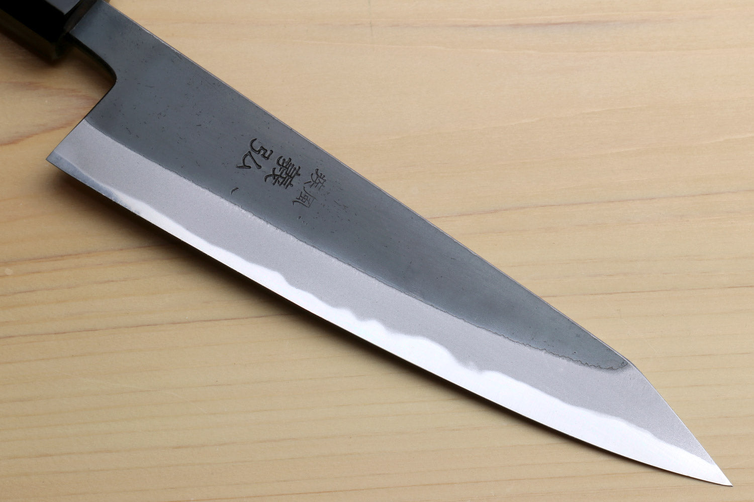 Kurouchi-finished blue steel knife blade angled view with engraved characters.