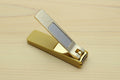 Gold-colored nail clipper with silver textured blade and lever.