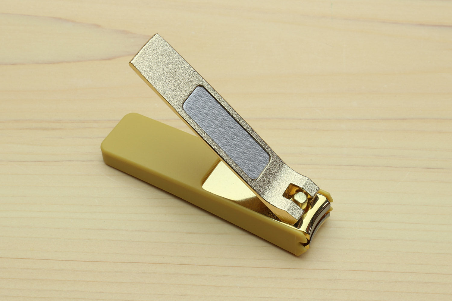 Gold-colored nail clipper with silver textured blade and lever.