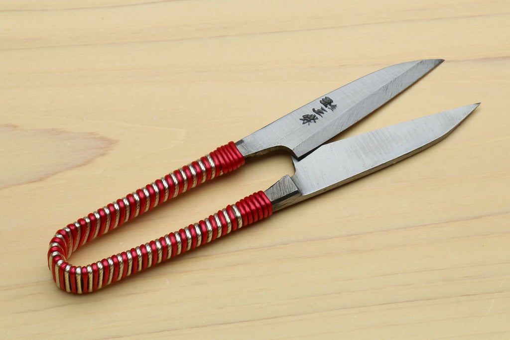 Japanese sewing snip scissors on light wood, red braided string-wrapped handle